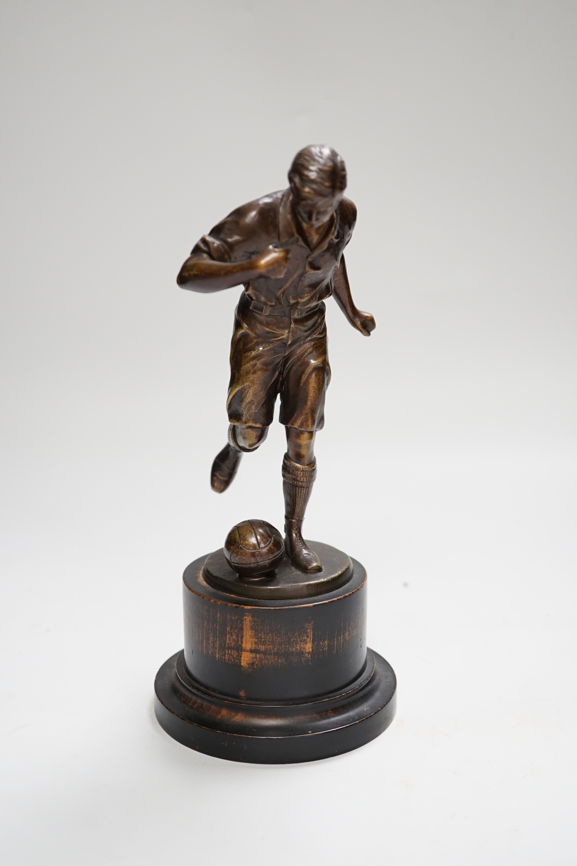 A pre-war bronze figure of a footballer, raised on a circular ebonies wood base, 23cm high